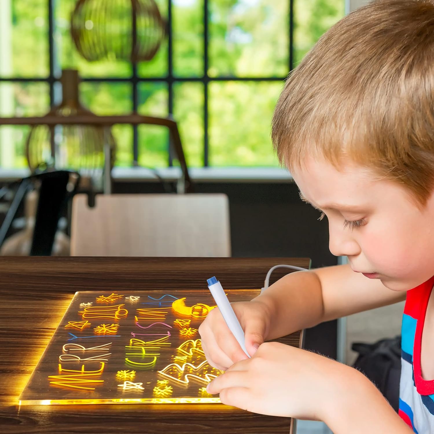 Child writing on a light-up board with colorful letters in a bright room.