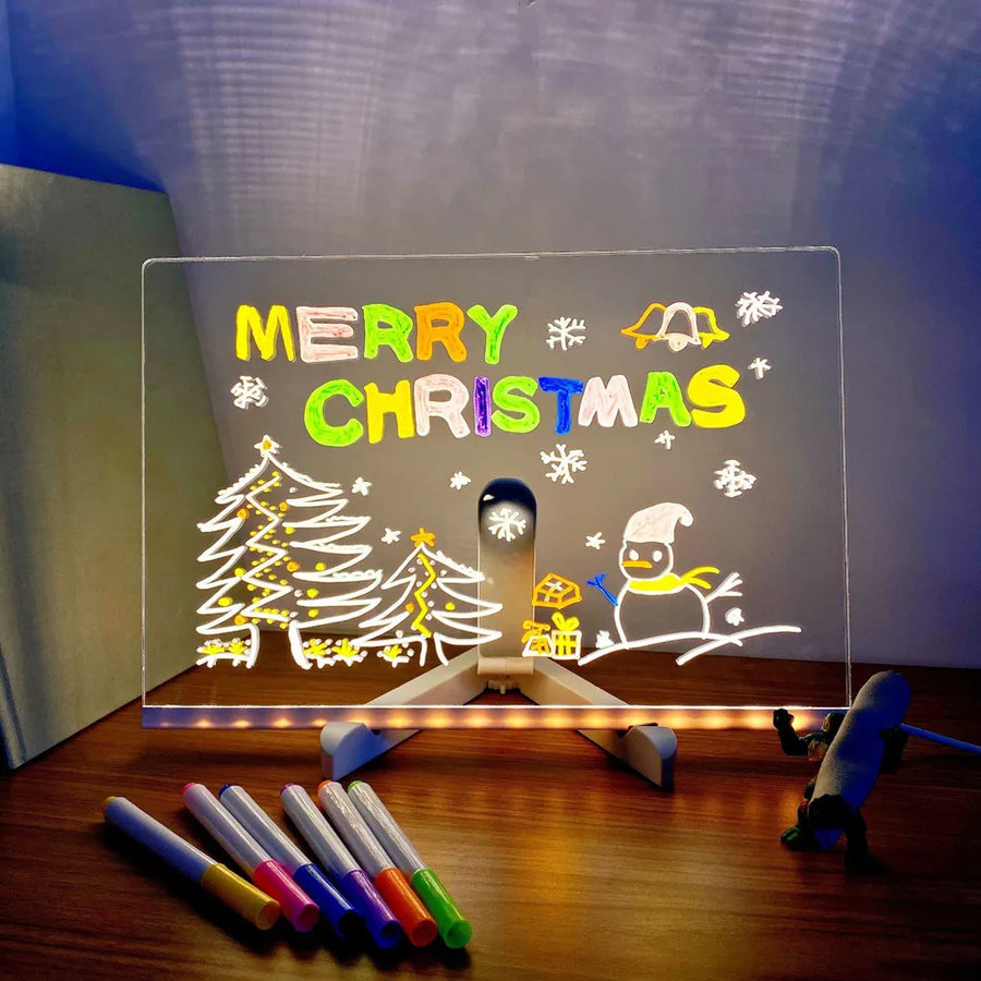 Transparent board with 'Merry Christmas' text and drawings on a stand, illuminated by LED lights.